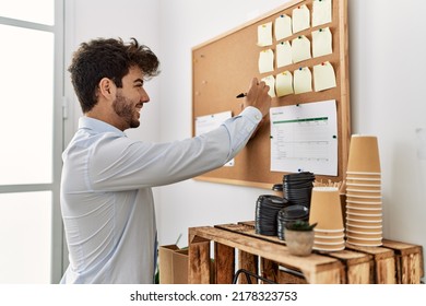 Young Hispanic Businessman Smiling Happy Writing On Cork Board At The Office.