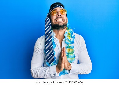 Young hispanic businessman wearing party funny style with tie on head begging and praying with hands together with hope expression on face very emotional and worried. begging. 