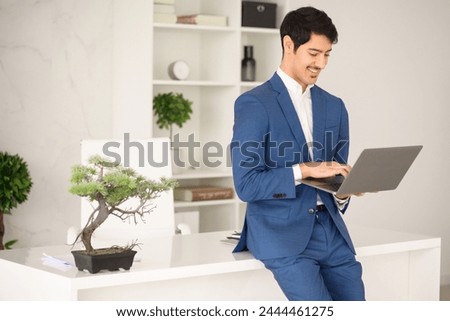 Young Hispanic businessman works attentively on his laptop, fully engaged in his task amidst a tastefully decorated office, represents dedication and seamless integration of technology in business