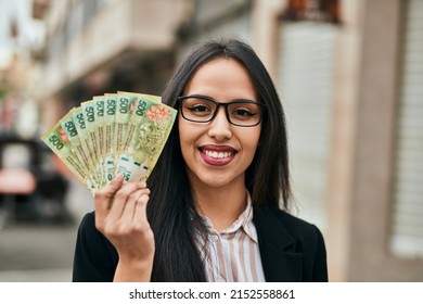 Young hispanic businesswoman holding argentina pesos banknotes at the city.