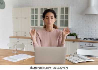 Young Hispanic businesswoman sit at table in kitchen near computer closed eyes makes breathing technique calming exercises. Stress management, anxiety relief due business problem. Self-control concept