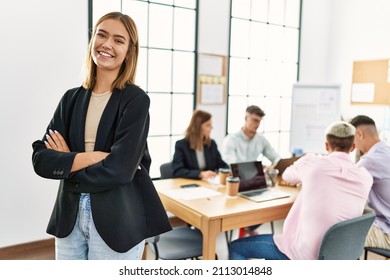 Young hispanic businesswoman smiling happy standing with arms crossed gesture at the office during business meeting.
