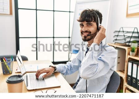 Young hispanic call center agent man smiling happy working at the office.