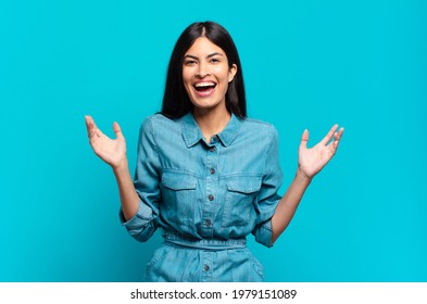 young hispanic casual woman feeling happy, excited, surprised or shocked, smiling and astonished at something unbelievable