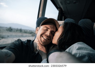 A young Hispanic and Caucasian couple are taking a selfie with a kiss on the cheek during a bus trip - Powered by Shutterstock