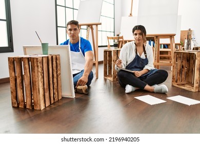 Young Hispanic Couple At Art Studio Thinking Attitude And Sober Expression Looking Self Confident 