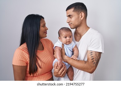 Young Hispanic Couple With Baby Standing Together Over Isolated Background Looking To Side, Relax Profile Pose With Natural Face And Confident Smile. 