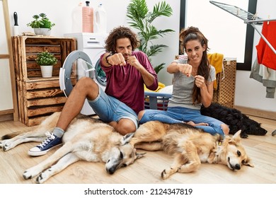 Young hispanic couple doing laundry with dogs punching fist to fight, aggressive and angry attack, threat and violence 