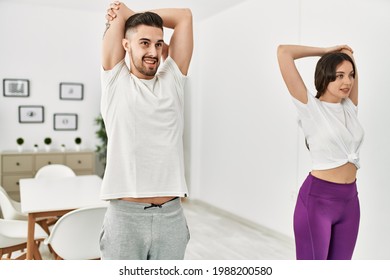 Young Hispanic Couple Doing Sport Streching Arms At Home