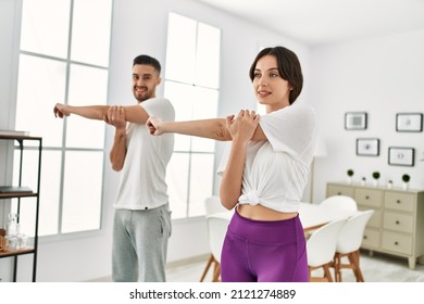 Young Hispanic Couple Doing Sport Streching Arms At Home