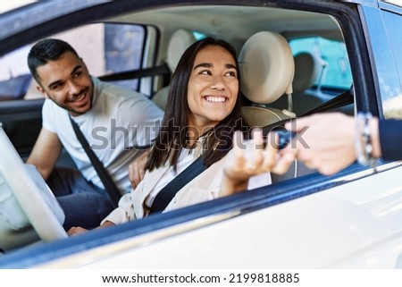 Young hispanic couple driving auto at the city. Girl smiling happy holding key of new car.