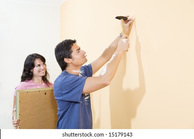 Young Hispanic Couple Hanging Picture On Wall