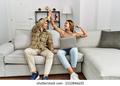 Young hispanic couple high five using laptop sitting on the sofa at home. - Shutterstock ID 2152846633