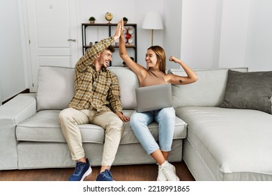 Young hispanic couple high five using laptop sitting on the sofa at home. - Shutterstock ID 2218991865