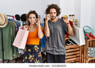 Young hispanic couple holding shopping bags at retail shop mouth and lips shut as zip with fingers. secret and silent, taboo talking 