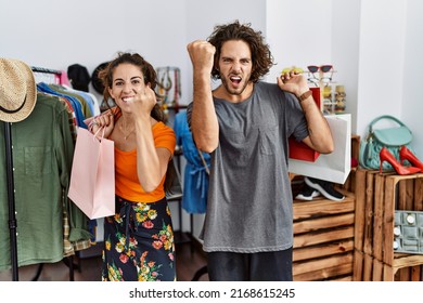 Young Hispanic Couple Holding Shopping Bags At Retail Shop Angry And Mad Raising Fist Frustrated And Furious While Shouting With Anger. Rage And Aggressive Concept. 