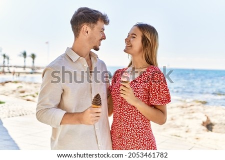 Young hispanic couple on vacation smiling happy eating ice cream at the beach