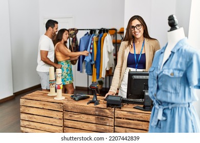 Young Hispanic Couple Shopping At Clothes Store. Shopkeeper Woman Smiling Happy Standing By Fashion Shop Counter.