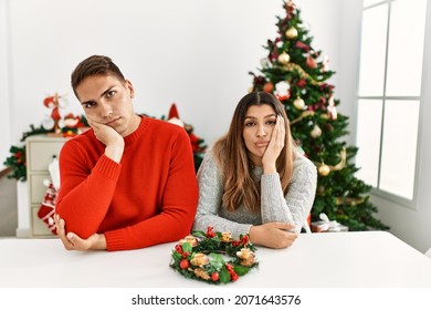 Young Hispanic Couple Sitting At The Table On Christmas Thinking Looking Tired And Bored With Depression Problems With Crossed Arms. 