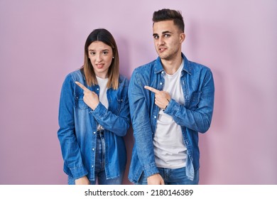 Young Hispanic Couple Standing Over Pink Background Pointing Aside Worried And Nervous With Forefinger, Concerned And Surprised Expression 