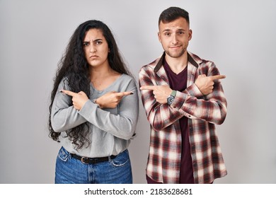 Young Hispanic Couple Standing Over White Background Pointing To Both Sides With Fingers, Different Direction Disagree 