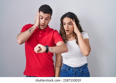 Young Hispanic Couple Standing Over Isolated Background Looking At The Watch Time Worried, Afraid Of Getting Late 