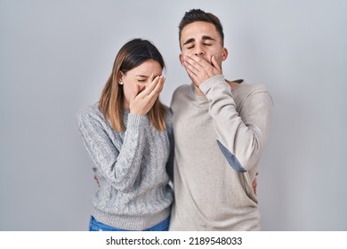 Young Hispanic Couple Standing Over White Background Bored Yawning Tired Covering Mouth With Hand. Restless And Sleepiness. 