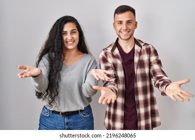 Young Hispanic Couple Standing Over White Background Smiling Cheerful Offering Hands Giving Assistance And Acceptance. 