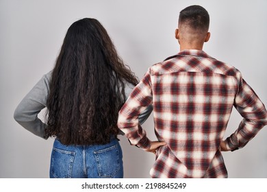 Young Hispanic Couple Standing Over White Background Standing Backwards Looking Away With Arms On Body 