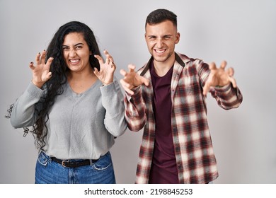 Young Hispanic Couple Standing Over White Background Smiling Funny Doing Claw Gesture As Cat, Aggressive And Sexy Expression 