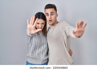 Young Hispanic Couple Standing Over White Background Doing Stop Gesture With Hands Palms, Angry And Frustration Expression 