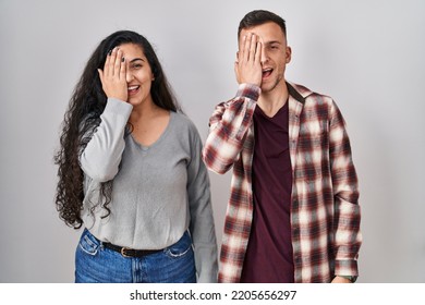 Young Hispanic Couple Standing Over White Background Covering One Eye With Hand, Confident Smile On Face And Surprise Emotion. 