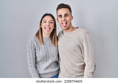 Young Hispanic Couple Standing Over White Background Sticking Tongue Out Happy With Funny Expression. Emotion Concept. 