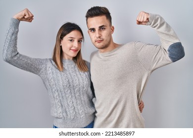 Young Hispanic Couple Standing Over White Background Strong Person Showing Arm Muscle, Confident And Proud Of Power 