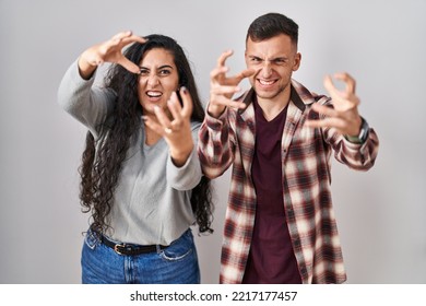 Young Hispanic Couple Standing Over White Background Shouting Frustrated With Rage, Hands Trying To Strangle, Yelling Mad 