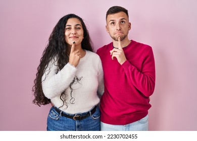 Young hispanic couple standing over pink background thinking concentrated about doubt with finger on chin and looking up wondering  - Shutterstock ID 2230702455