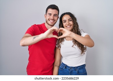 Young hispanic couple standing over isolated background smiling in love doing heart symbol shape with hands. romantic concept.  - Shutterstock ID 2235686229