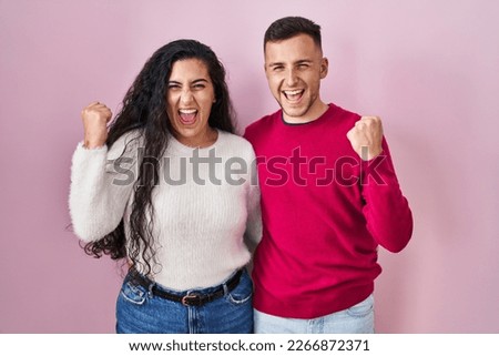 Young hispanic couple standing over pink background very happy and excited doing winner gesture with arms raised, smiling and screaming for success. celebration concept.  Foto d'archivio © 
