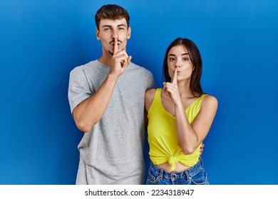 Young hispanic couple standing together over blue background asking to be quiet with finger on lips. silence and secret concept.  - Shutterstock ID 2234318947