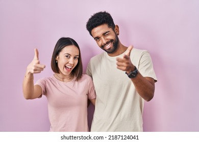 Young hispanic couple together over pink background pointing fingers to camera with happy and funny face. good energy and vibes.  - Powered by Shutterstock