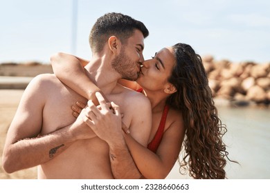 Young hispanic couple tourists wearing swimsuit hugging each other and kissing at seaside - Powered by Shutterstock