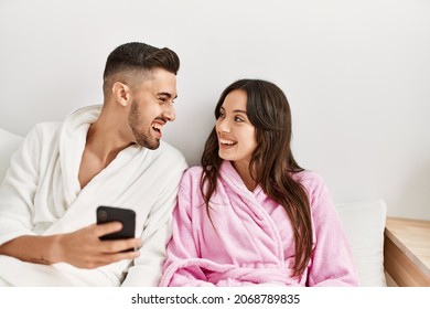 Young hispanic couple using smartphone lying on bed at home.