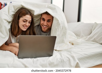 Young Hispanic Couple Watching Movie Using Laptop Lying In Bed.