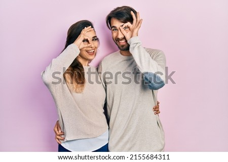Young hispanic couple wearing casual clothes doing ok gesture with hand smiling, eye looking through fingers with happy face. 