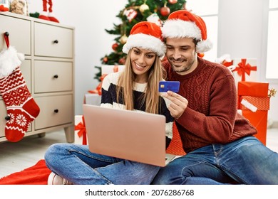Young hispanic couple wearing christmas hat buying using laptop and credit card at home.