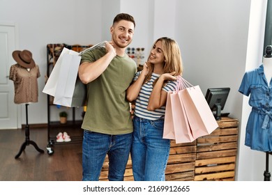 Young hispanic customer couple smiling happy holding shopping bags at clothing store. - Powered by Shutterstock