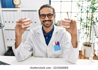 Young Hispanic Dentist Man Holding Denture With Orthodontic Braces Smiling With A Happy And Cool Smile On Face. Showing Teeth. 