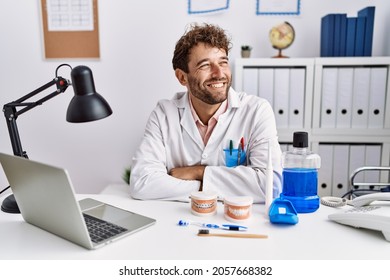 Young Hispanic Dentist Man Working At Medical Clinic Looking Away To Side With Smile On Face, Natural Expression. Laughing Confident. 