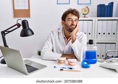 Young hispanic dentist man working at medical clinic thinking looking tired and bored with depression problems with crossed arms. 