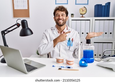 Young Hispanic Dentist Man Working At Medical Clinic Amazed And Smiling To The Camera While Presenting With Hand And Pointing With Finger. 